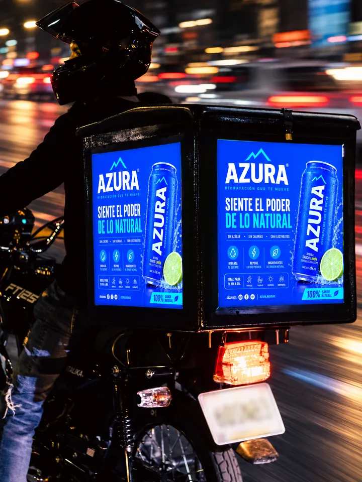 Caja iluminada con el anuncio de una bebida, en una moto circulando de noche