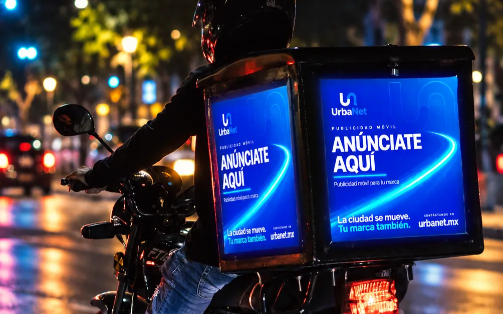 Caja iluminada de Urbanet con el mensaje Anúnciate aquí, en una moto de noche